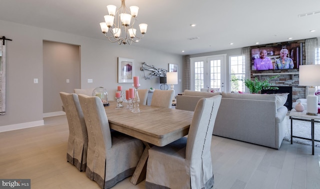 dining room featuring a barn door, a fireplace, a chandelier, and light hardwood / wood-style floors