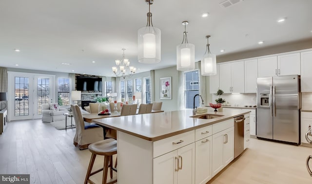 kitchen with sink, hanging light fixtures, stainless steel appliances, a kitchen island with sink, and white cabinets