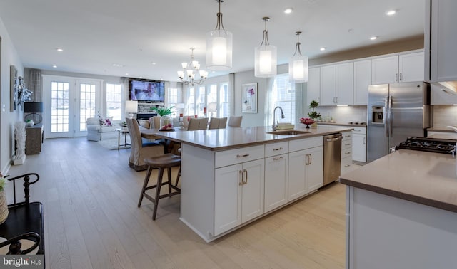 kitchen with sink, hanging light fixtures, appliances with stainless steel finishes, an island with sink, and white cabinets