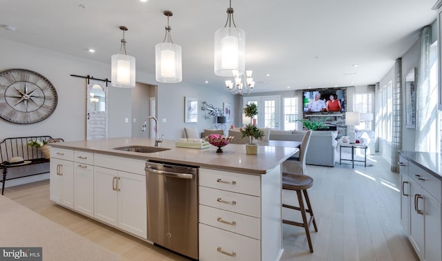 kitchen featuring hanging light fixtures, dishwasher, a barn door, and an island with sink