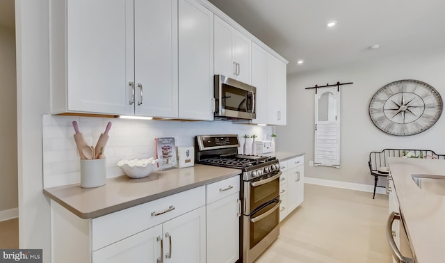 kitchen with decorative backsplash, stainless steel appliances, a barn door, and white cabinets