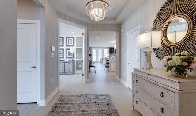 hall featuring an inviting chandelier, a raised ceiling, and light hardwood / wood-style floors