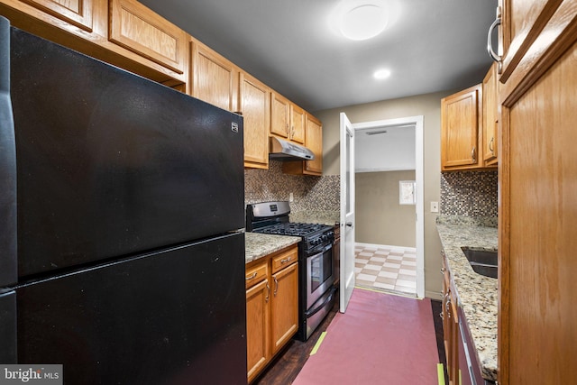 kitchen featuring decorative backsplash, stainless steel gas range, light stone countertops, and black fridge