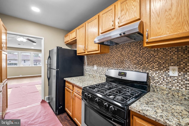 kitchen with black fridge, light stone counters, backsplash, and range with gas cooktop