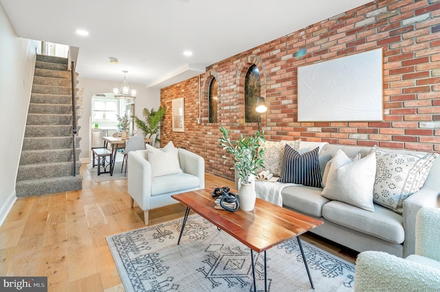 living room with a notable chandelier, light hardwood / wood-style floors, and brick wall