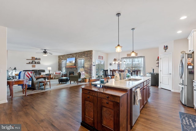 kitchen with sink, a stone fireplace, appliances with stainless steel finishes, a kitchen island with sink, and decorative light fixtures