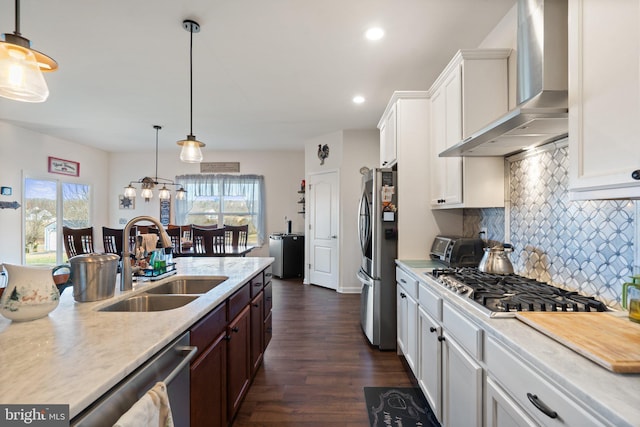 kitchen with wall chimney exhaust hood, sink, hanging light fixtures, appliances with stainless steel finishes, and white cabinets