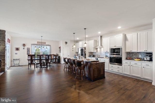 kitchen with white cabinetry, pendant lighting, a center island with sink, and wall chimney exhaust hood