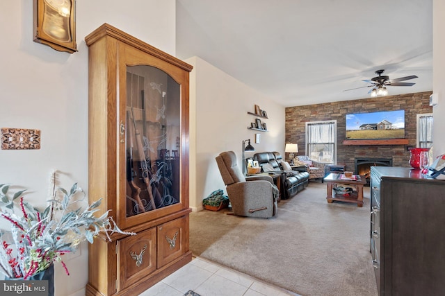 carpeted living room with a stone fireplace and ceiling fan