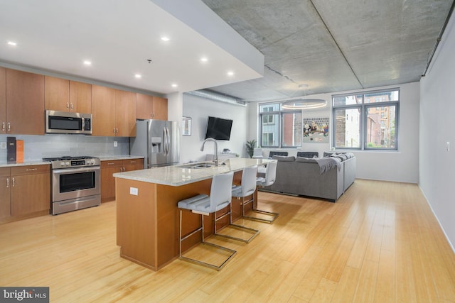 kitchen with sink, appliances with stainless steel finishes, a kitchen breakfast bar, light hardwood / wood-style floors, and an island with sink