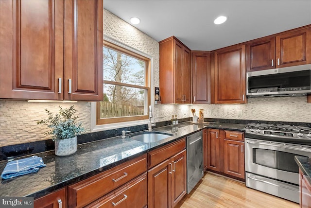 kitchen with sink, tasteful backsplash, appliances with stainless steel finishes, dark stone counters, and light hardwood / wood-style floors