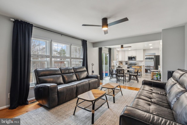 living area with ceiling fan, light wood finished floors, and baseboards