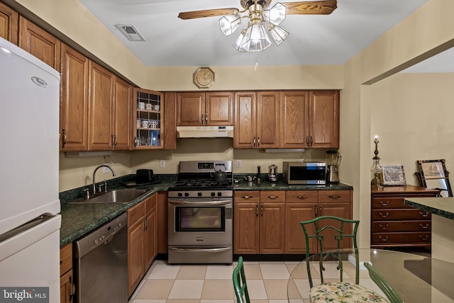 kitchen with sink, light tile patterned floors, appliances with stainless steel finishes, ceiling fan, and dark stone counters