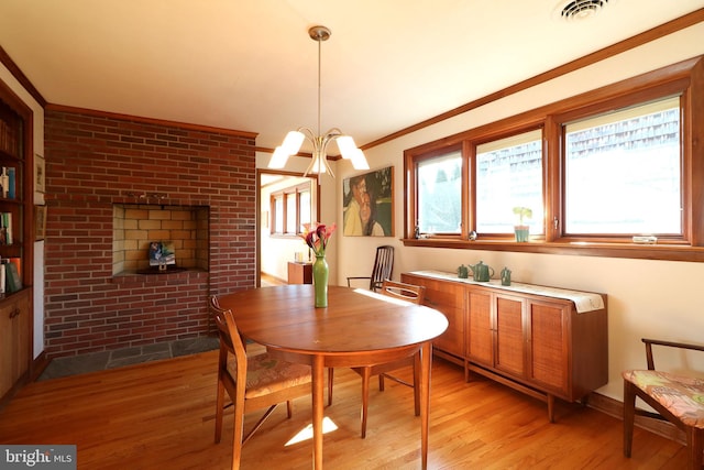 dining space with crown molding, a notable chandelier, brick wall, and light wood-type flooring