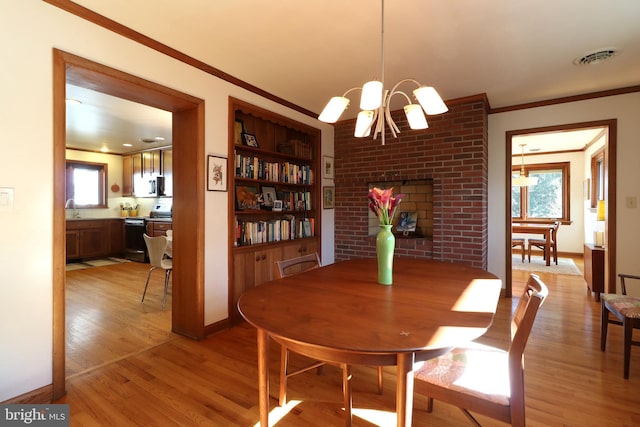 dining room featuring built in shelves, sink, light wood-type flooring, ornamental molding, and a notable chandelier