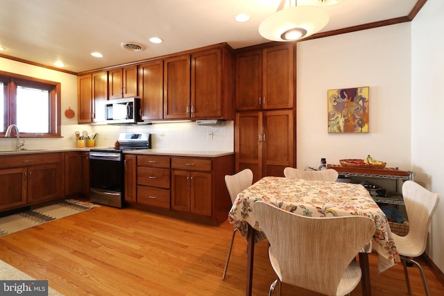 kitchen with appliances with stainless steel finishes, sink, light wood-type flooring, and decorative backsplash