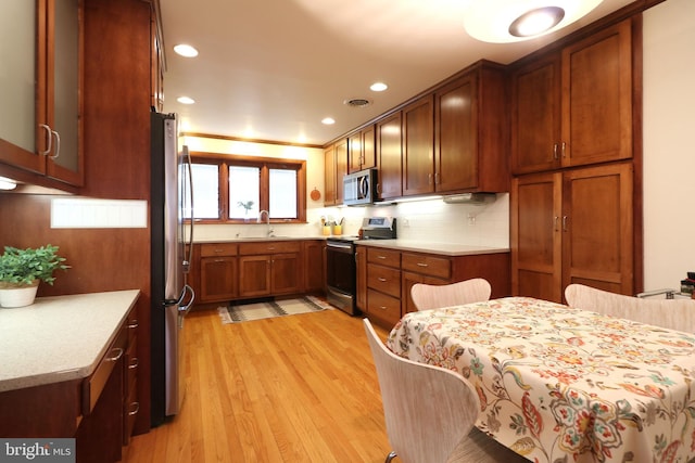 kitchen with sink, decorative backsplash, light wood-type flooring, and appliances with stainless steel finishes