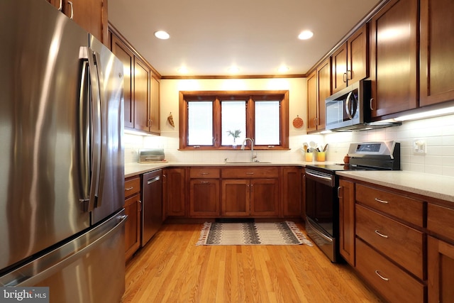 kitchen with tasteful backsplash, appliances with stainless steel finishes, sink, and light hardwood / wood-style floors