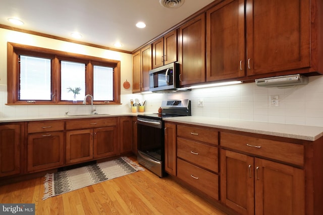 kitchen with sink, ornamental molding, stainless steel appliances, light hardwood / wood-style floors, and decorative backsplash