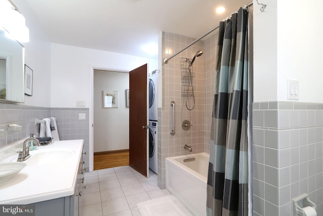 bathroom featuring stacked washer and clothes dryer, tile walls, vanity, shower / bath combo with shower curtain, and tile patterned flooring