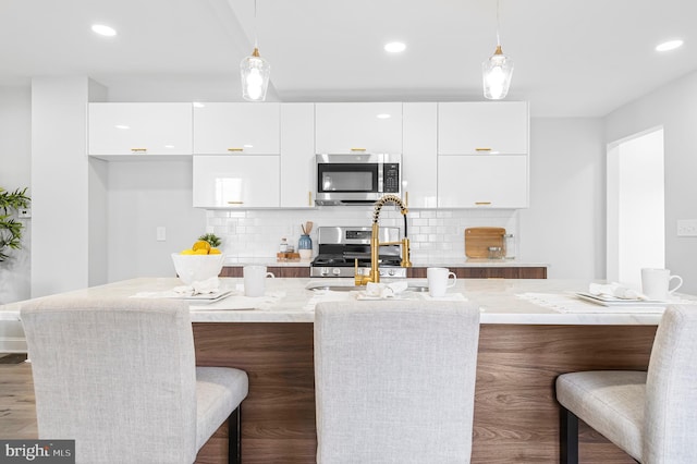 kitchen with light stone countertops, white cabinetry, appliances with stainless steel finishes, and pendant lighting