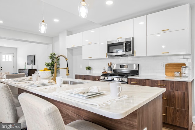 kitchen with sink, white cabinetry, hanging light fixtures, a center island with sink, and appliances with stainless steel finishes