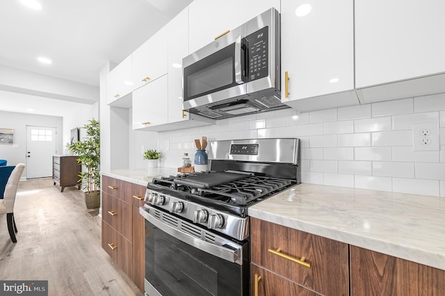 kitchen with appliances with stainless steel finishes, light stone counters, white cabinets, decorative backsplash, and light wood-type flooring