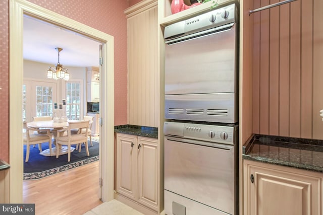 kitchen featuring stacked washer / dryer, light hardwood / wood-style floors, decorative light fixtures, oven, and dark stone counters