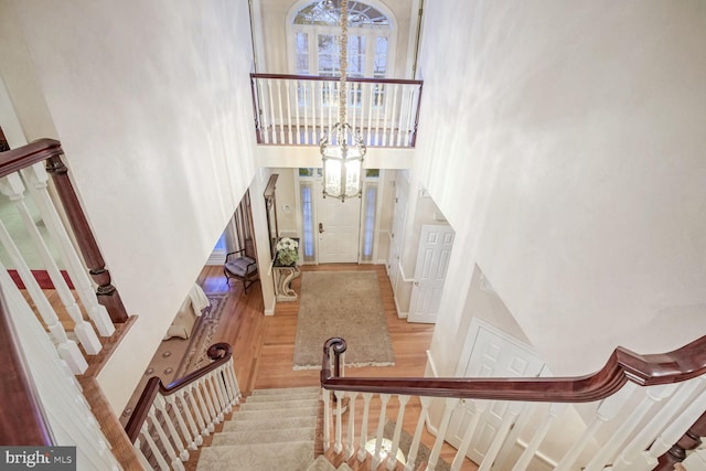 stairs with a towering ceiling, wood-type flooring, and a chandelier