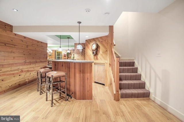 bar with decorative light fixtures, light hardwood / wood-style flooring, and wood walls