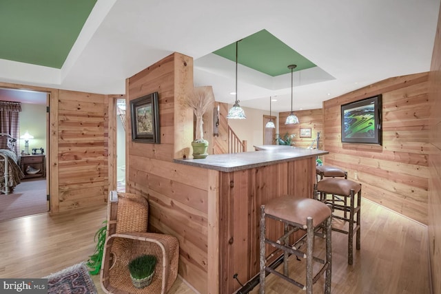 bar featuring a tray ceiling, decorative light fixtures, light wood-type flooring, and wood walls