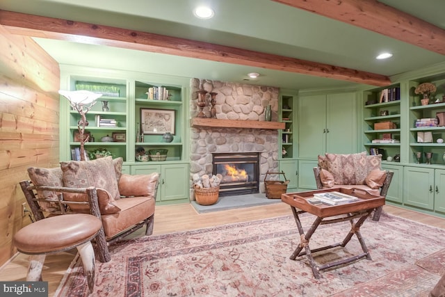 sitting room featuring beamed ceiling, wooden walls, a fireplace, and light hardwood / wood-style floors