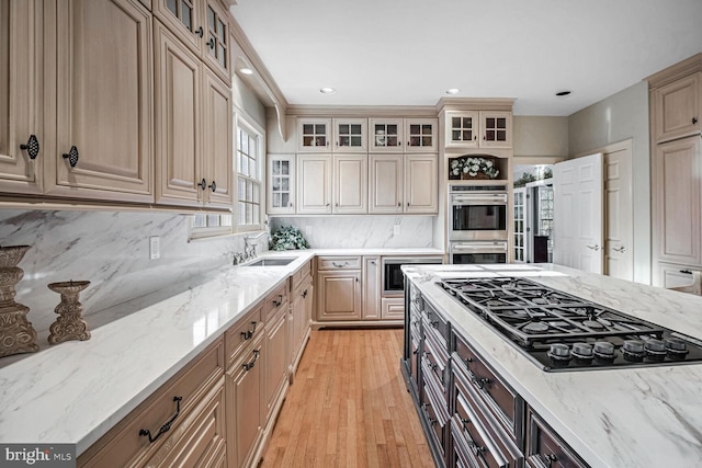 kitchen with sink, decorative backsplash, stainless steel appliances, light stone countertops, and light hardwood / wood-style flooring