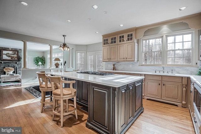 kitchen with sink, a center island, hanging light fixtures, light wood-type flooring, and decorative columns