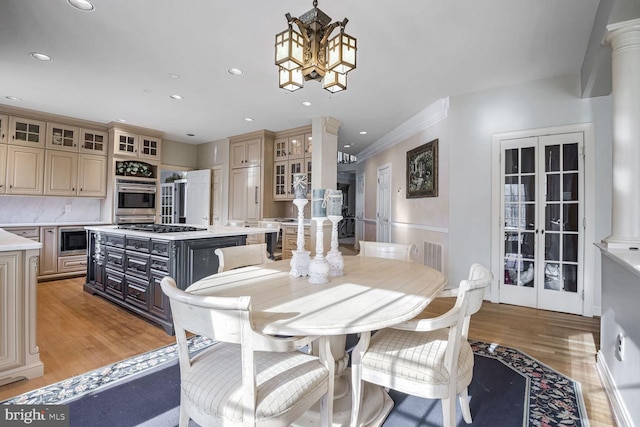 dining space with decorative columns, crown molding, a notable chandelier, and light hardwood / wood-style floors