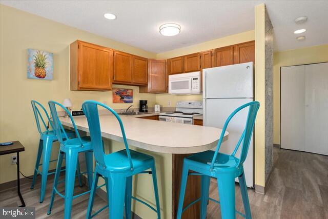 kitchen with dark hardwood / wood-style flooring, a kitchen bar, white appliances, and kitchen peninsula