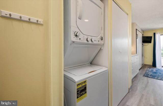 clothes washing area featuring stacked washing maching and dryer and light wood-type flooring