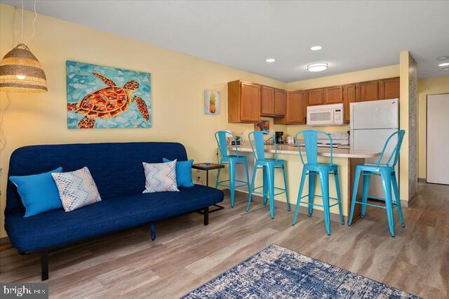 kitchen with white appliances, a kitchen bar, kitchen peninsula, and light hardwood / wood-style floors