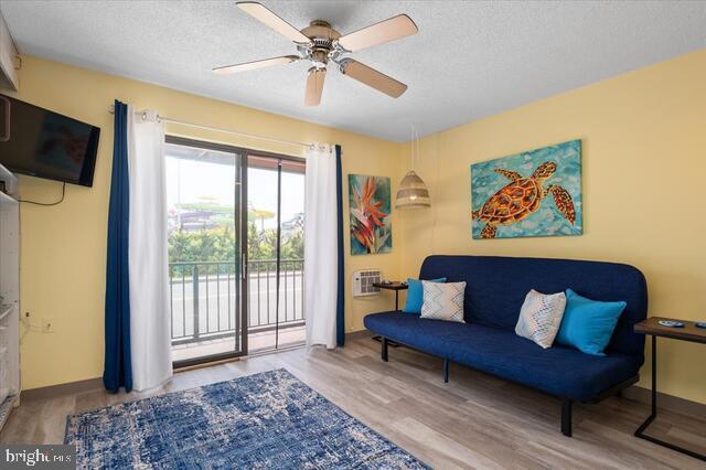 living area with ceiling fan, a wall mounted air conditioner, a textured ceiling, and light wood-type flooring