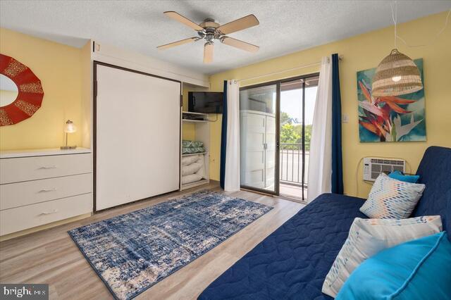 bedroom with a textured ceiling, light hardwood / wood-style flooring, access to outside, a closet, and a wall unit AC