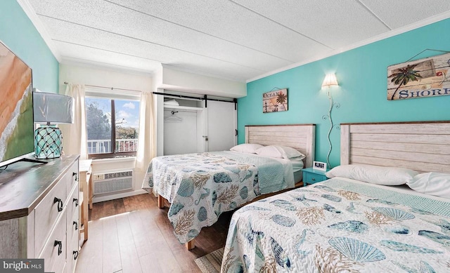 bedroom featuring an AC wall unit, ornamental molding, light hardwood / wood-style floors, a barn door, and a textured ceiling