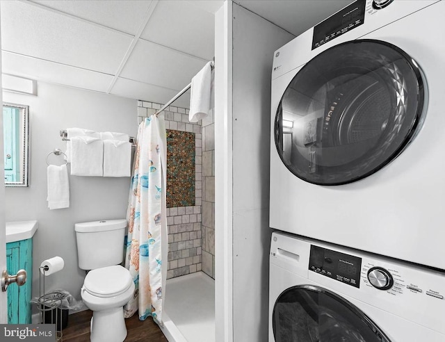 bathroom featuring walk in shower, stacked washing maching and dryer, hardwood / wood-style floors, and toilet