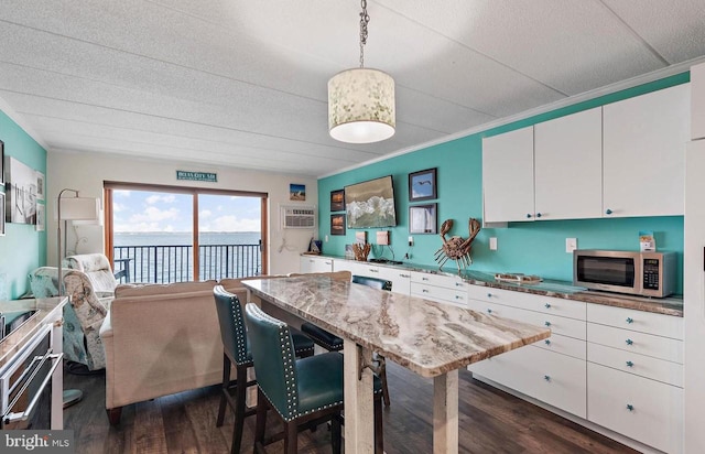 kitchen featuring pendant lighting, crown molding, white cabinetry, dark hardwood / wood-style floors, and a water view