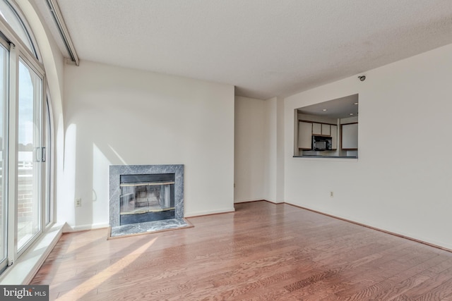 unfurnished living room with hardwood / wood-style floors, a wealth of natural light, a textured ceiling, and a fireplace