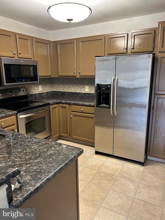 kitchen featuring dark stone countertops, light tile patterned floors, decorative backsplash, and appliances with stainless steel finishes