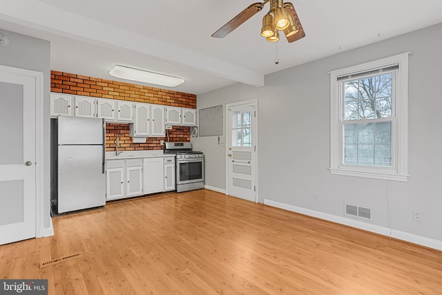 kitchen with stainless steel gas stove, light wood-type flooring, fridge, plenty of natural light, and white cabinets