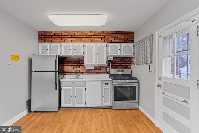 kitchen with sink, white cabinetry, appliances with stainless steel finishes, brick wall, and light hardwood / wood-style floors