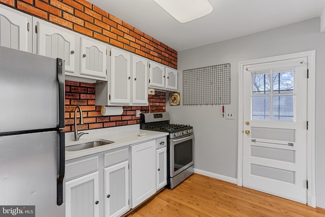 kitchen featuring stainless steel appliances, sink, brick wall, light hardwood / wood-style floors, and white cabinets