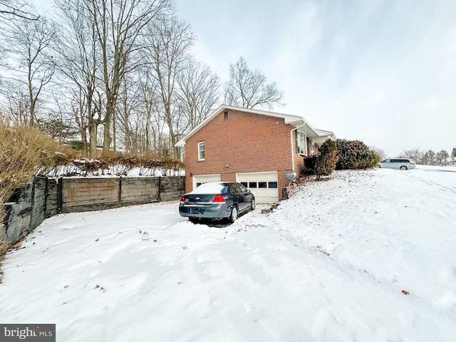 snow covered property featuring a garage, brick siding, and fence