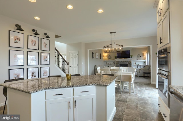 kitchen with stone countertops, white cabinetry, a kitchen island, decorative light fixtures, and stainless steel double oven